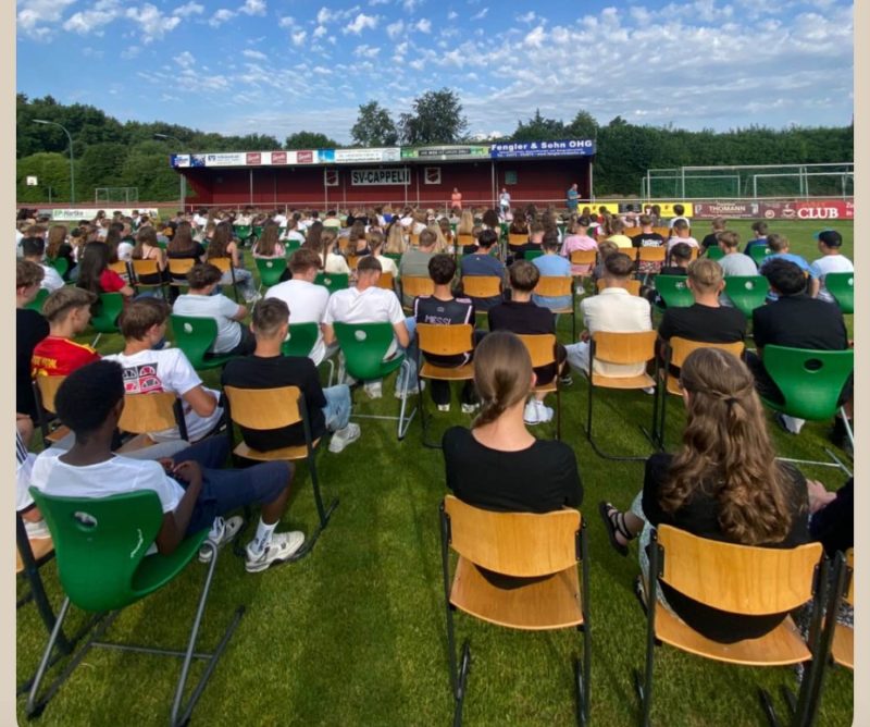 Bild zeigt Schülerinnen und Schüler sitzend auf einem Stuhl auf dem Sportplatz